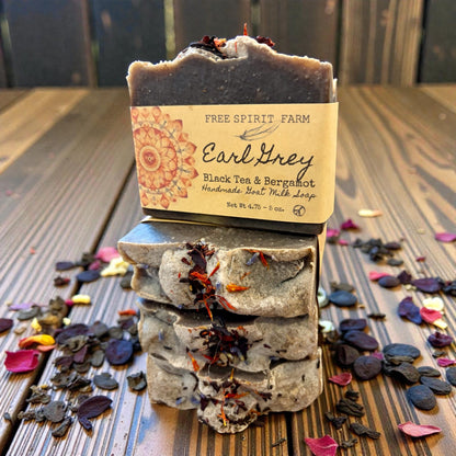 Stack of Earl Grey soap bars with a visible brand label on a wooden surface with tea leaves.