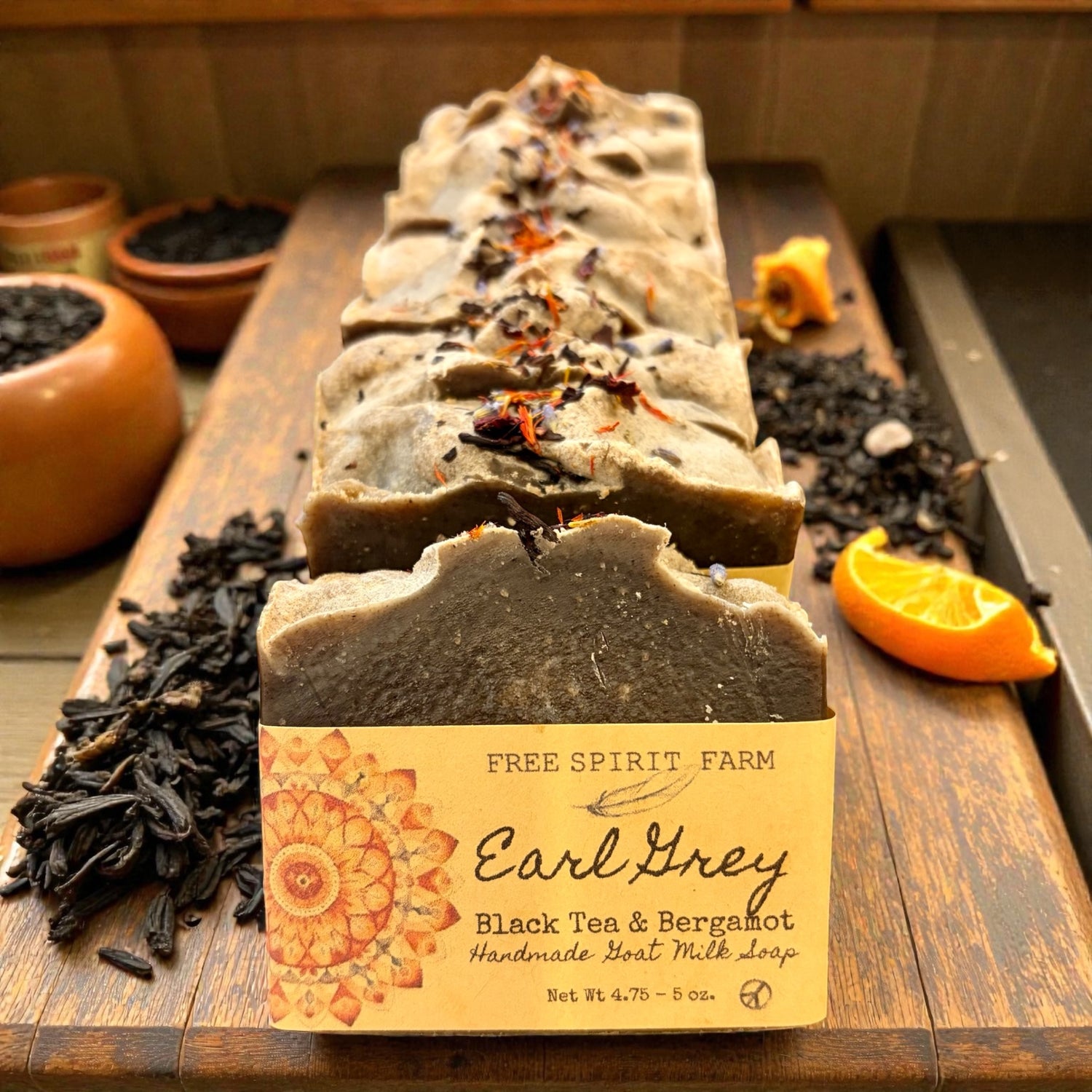 Row of Earl Grey soap bars with a Free Spirit Farm label on a wooden surface with tea leaves and an orange.