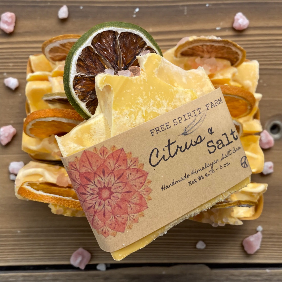 Bar of soap with a decorative label on a wooden surface with citrus slices and pink flowers.