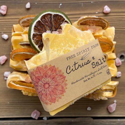 Bar of soap with a decorative label on a wooden surface with citrus slices and pink flowers.