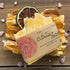 Bar of soap with a decorative label on a wooden surface with citrus slices and pink flowers.