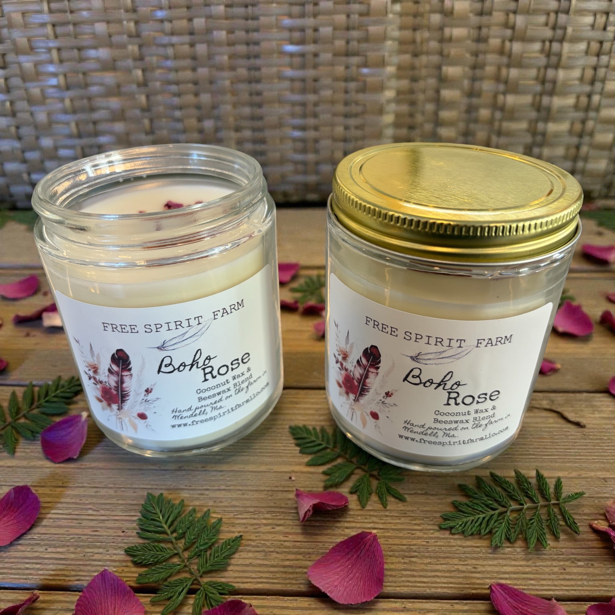 Two candles from Free Spirit Farm on a wooden surface with rose petals and leaves.