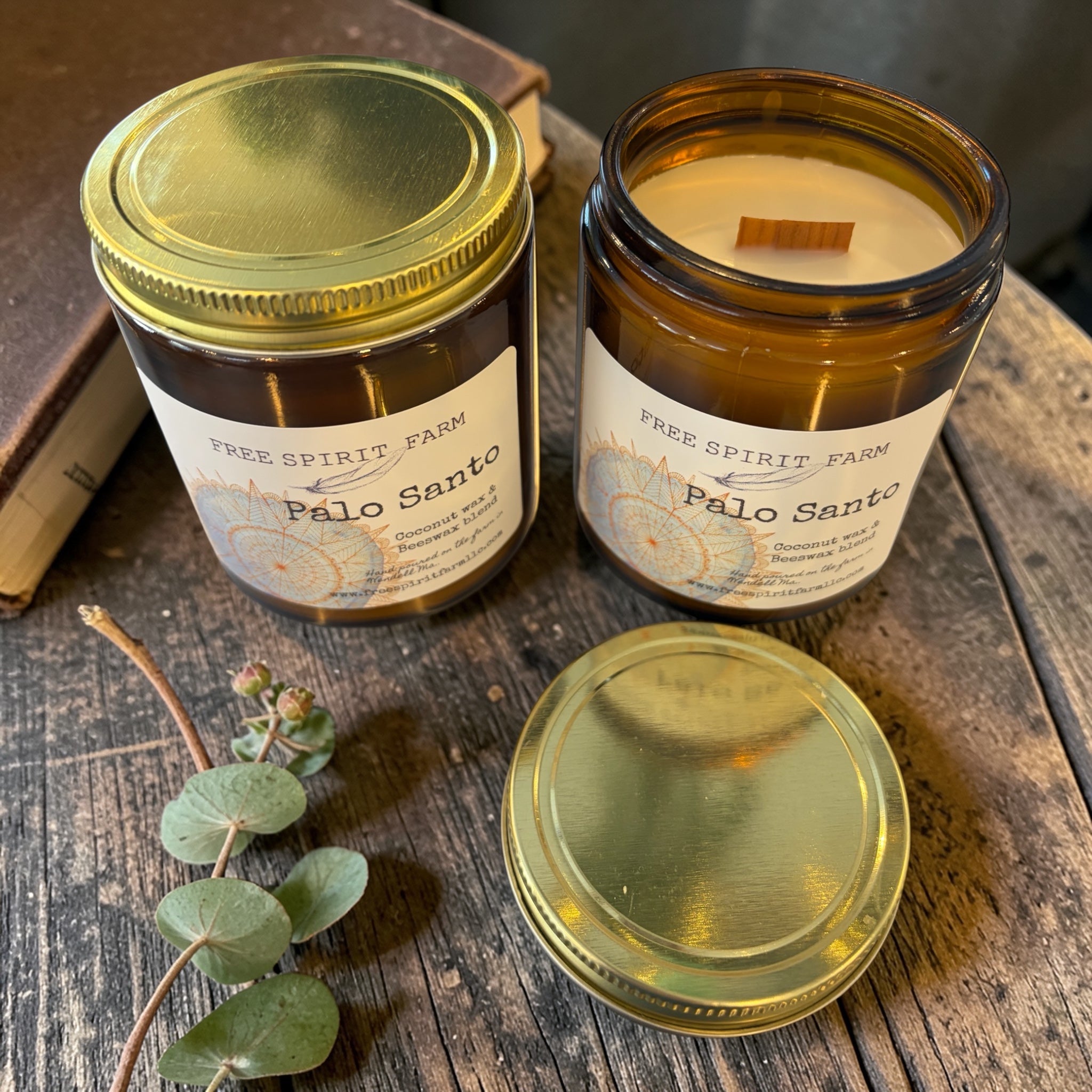 Two Palo Santo candles from Free Spirit Farm on a wooden surface with a branch of eucalyptus.