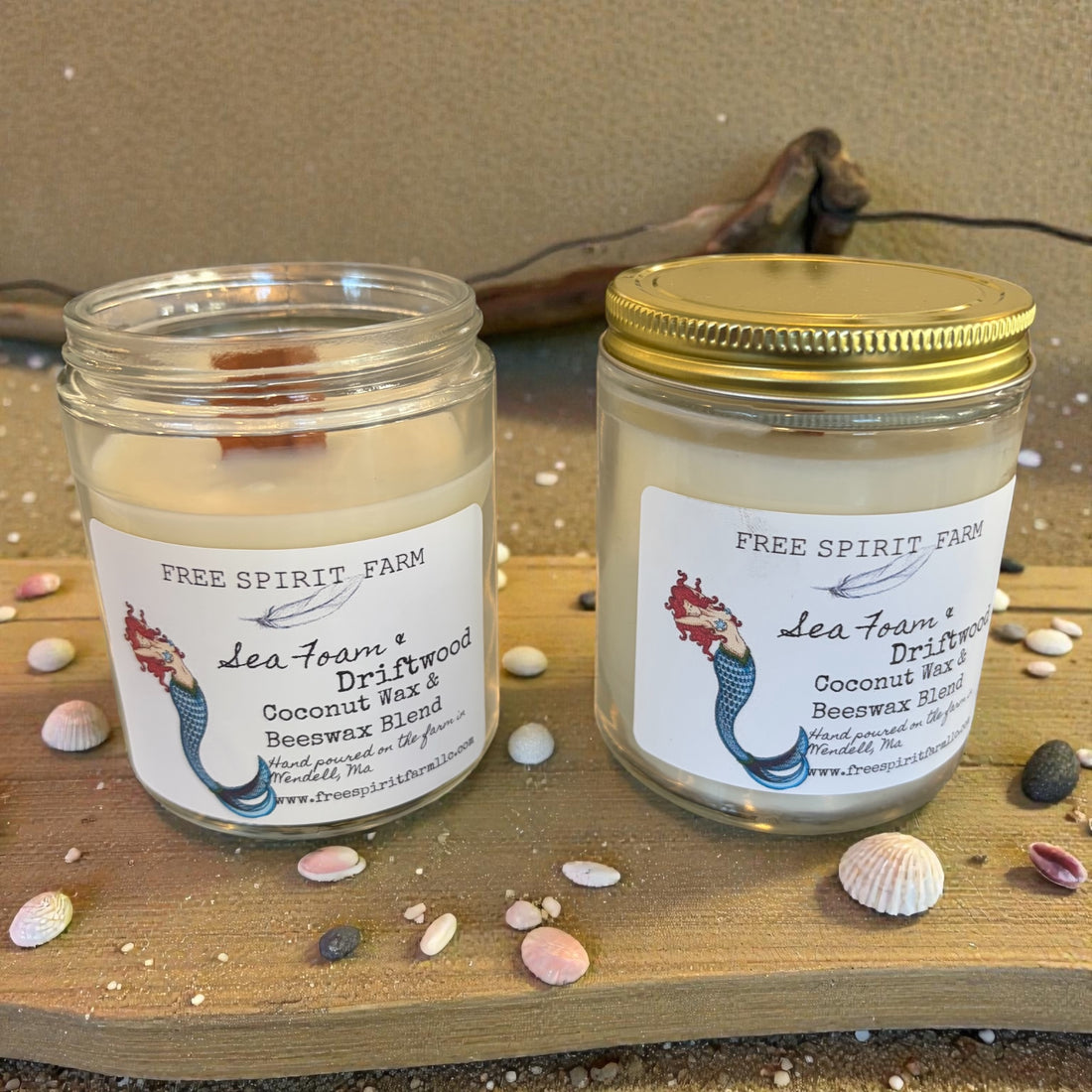 Two candles from Free Spirit Farm on a wooden surface with seashells.