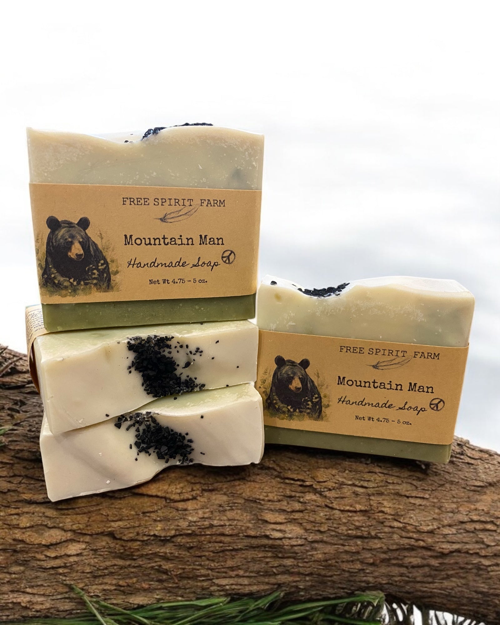 A bar of handmade vegan soap with a mountain man theme, featuring a beige color and black accents resembling soil or dirt, placed on a wooden surface with packaging in the background.