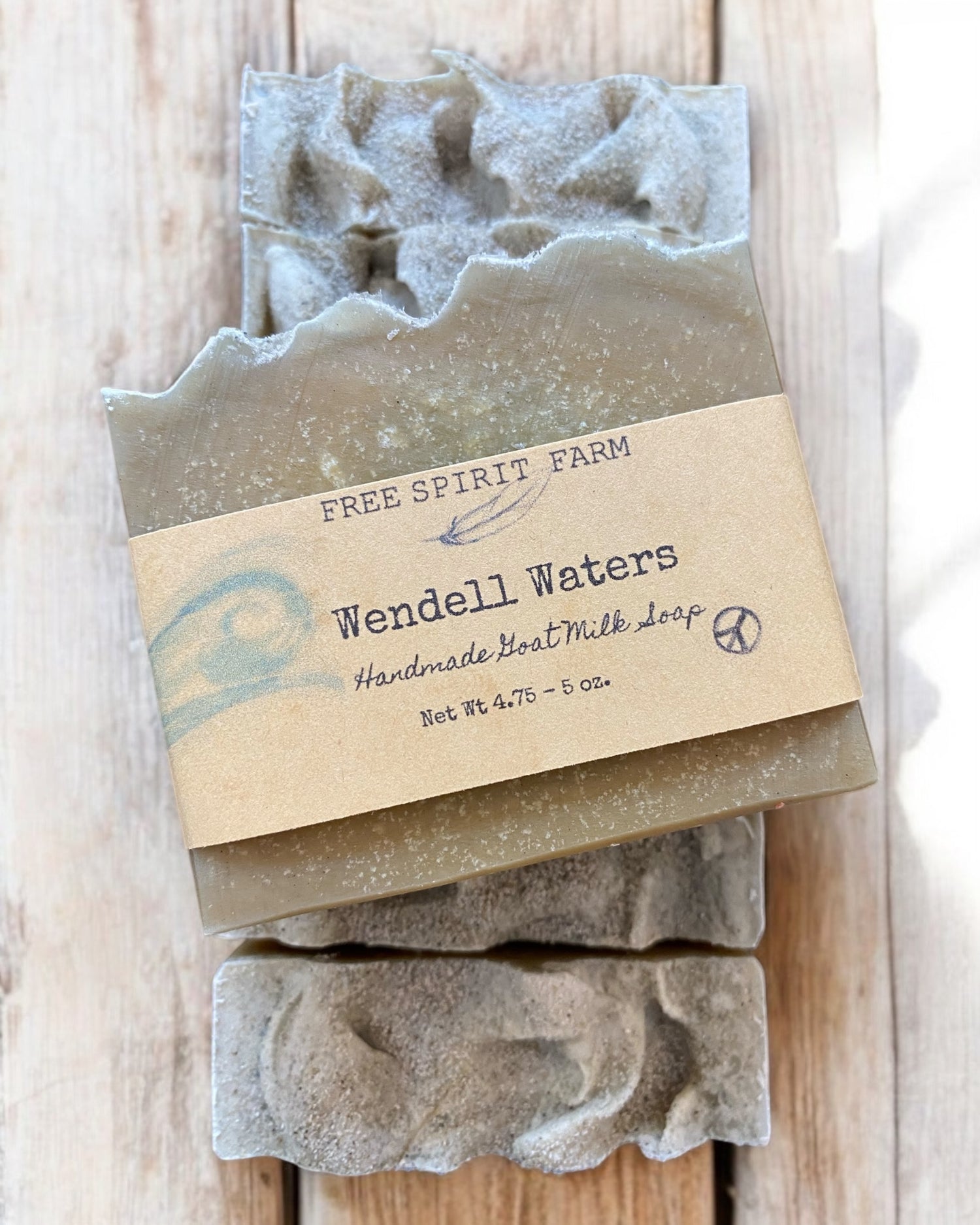 A bar of goat milk soap with exfoliating pumice on top, wrapped in a paper labeled &