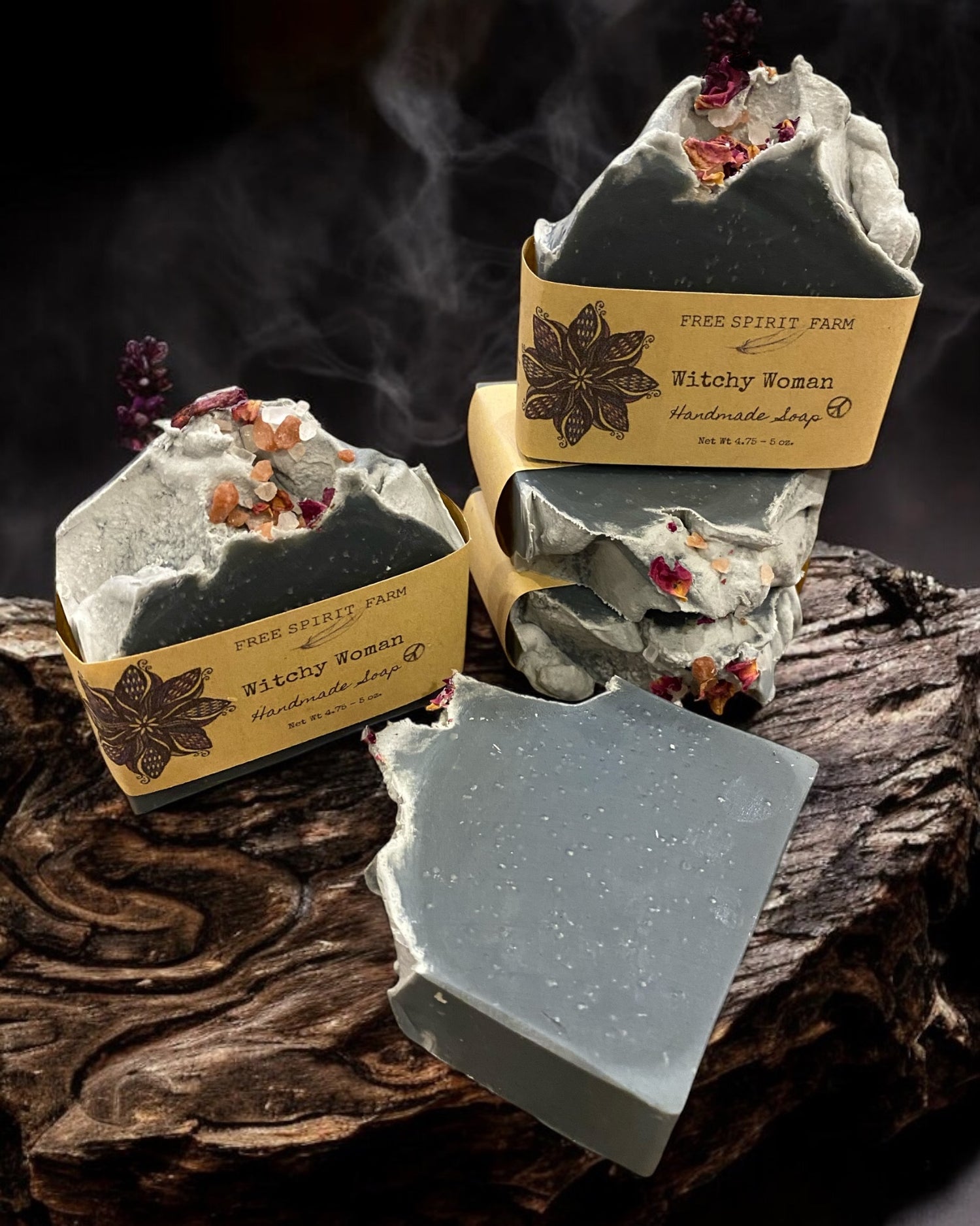 A bar of soap with a grayish color and decorative elements on top, placed on a rustic wooden surface with soap bars in the background.
