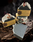 A bar of soap with a grayish color and decorative elements on top, placed on a rustic wooden surface with soap bars in the background.