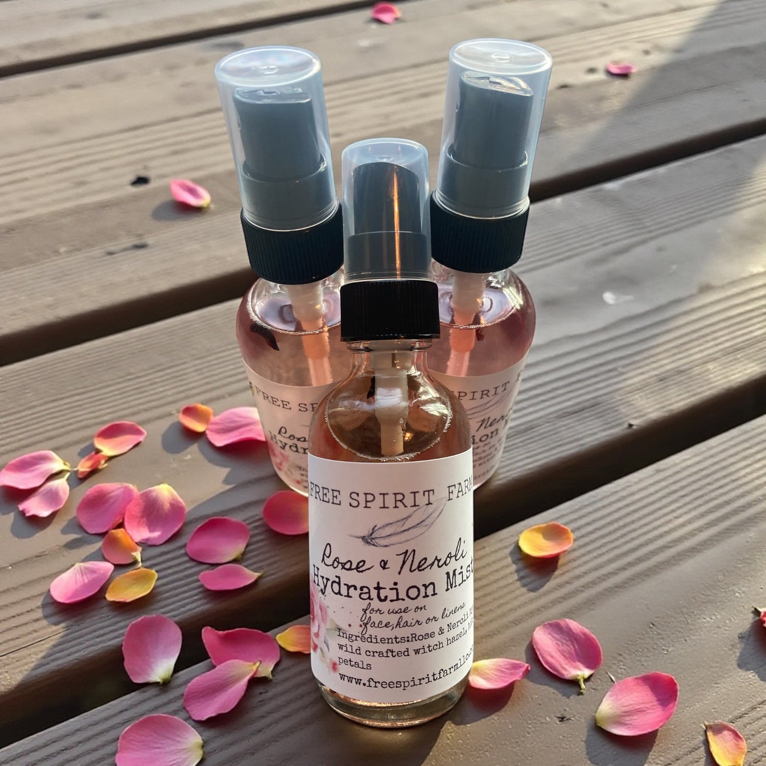 Three small spray bottles with a label on a wooden surface with pink petals.