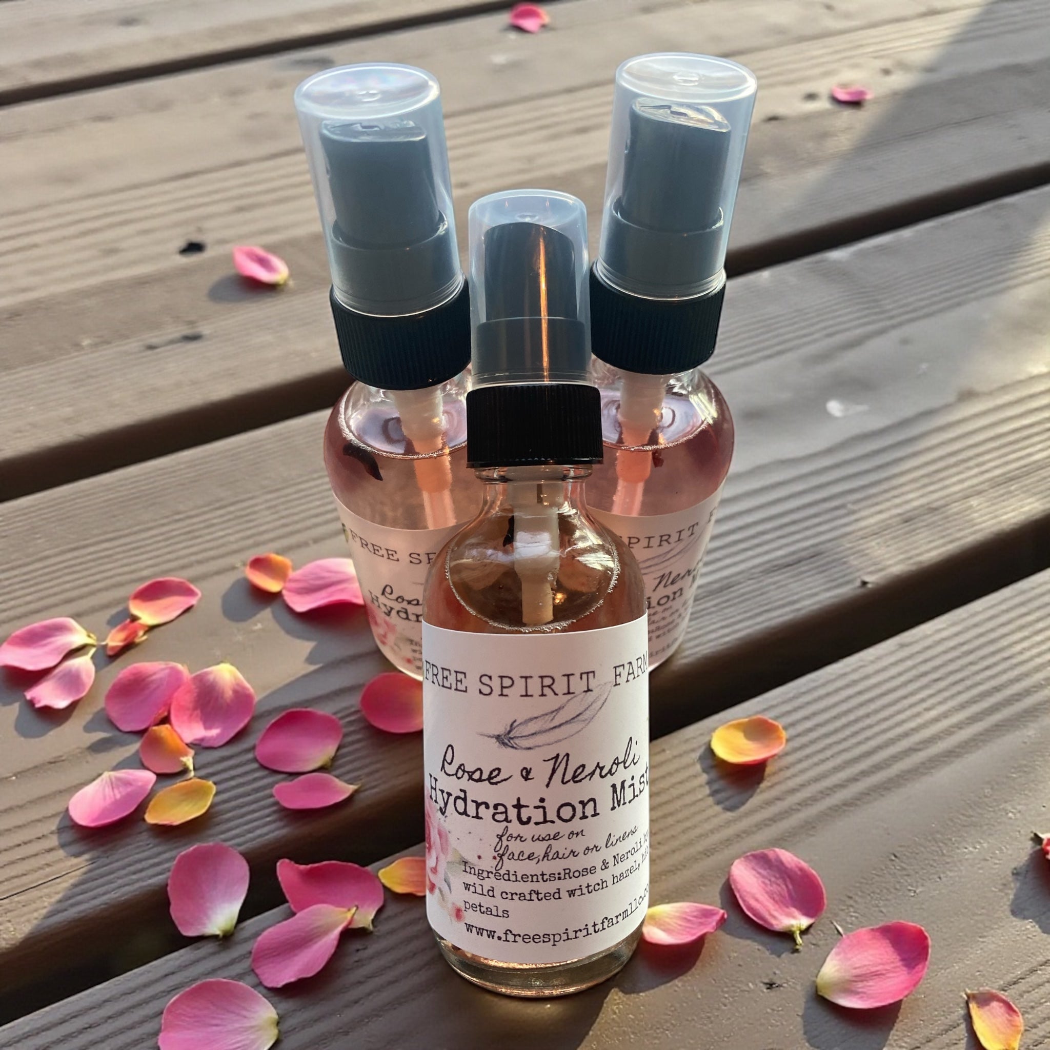 Three small spray bottles with a label on a wooden surface with pink petals.