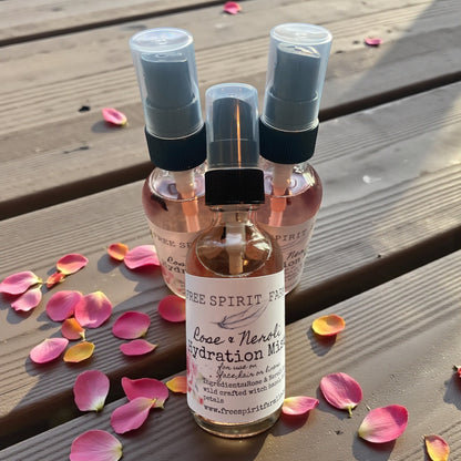 Three small spray bottles with a label on a wooden surface with pink petals.