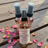 Three small spray bottles with a label on a wooden surface with pink petals.