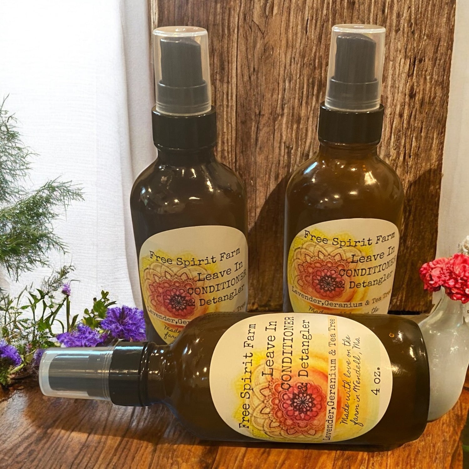 Three bottles of Free Spirit Farm Leave In Conditioner on a wooden surface with flowers in the background.