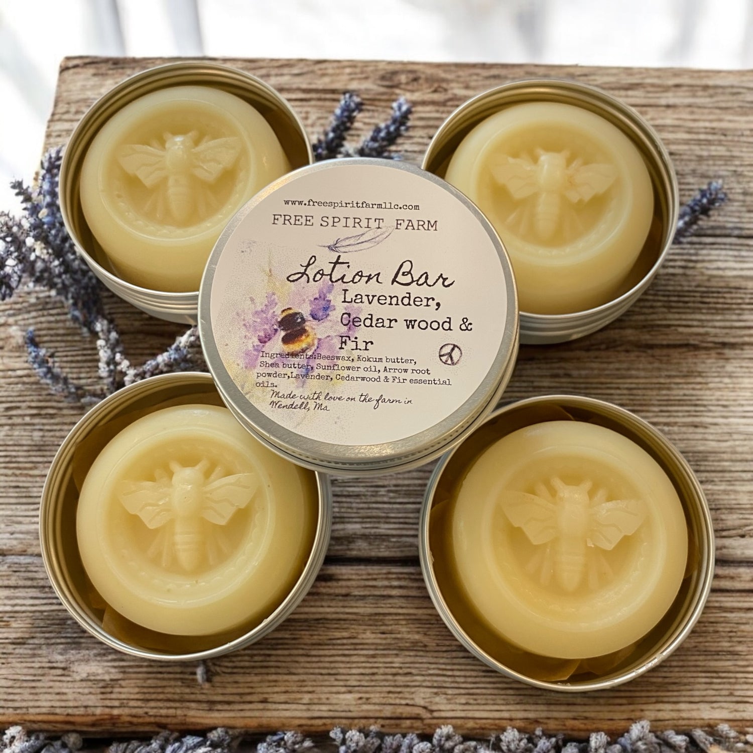 Four tins of Free Spirit Farm lotion bars on a wooden surface with lavender flowers.