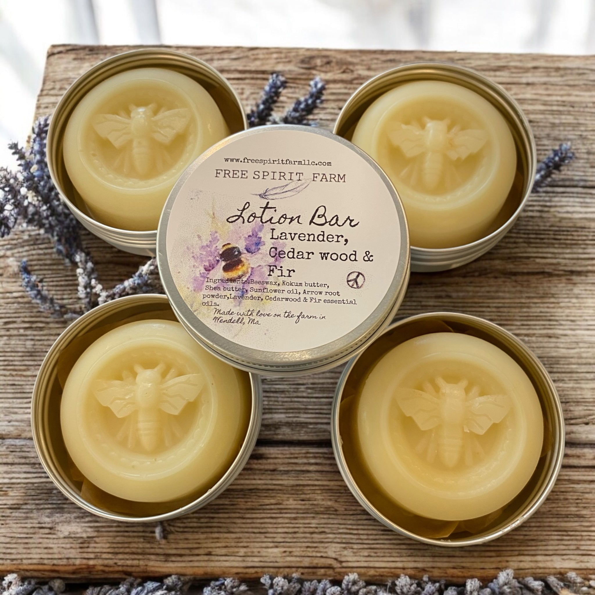 Four tins of Free Spirit Farm lotion bars on a wooden surface with lavender flowers.