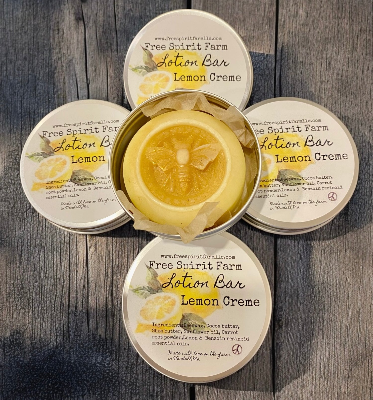 Three jars of Free Spirit Farm Lotion Bar Lemon Crème with a decorative bee on the lid of one jar, placed on a wooden surface with a lemon slice in the center.
