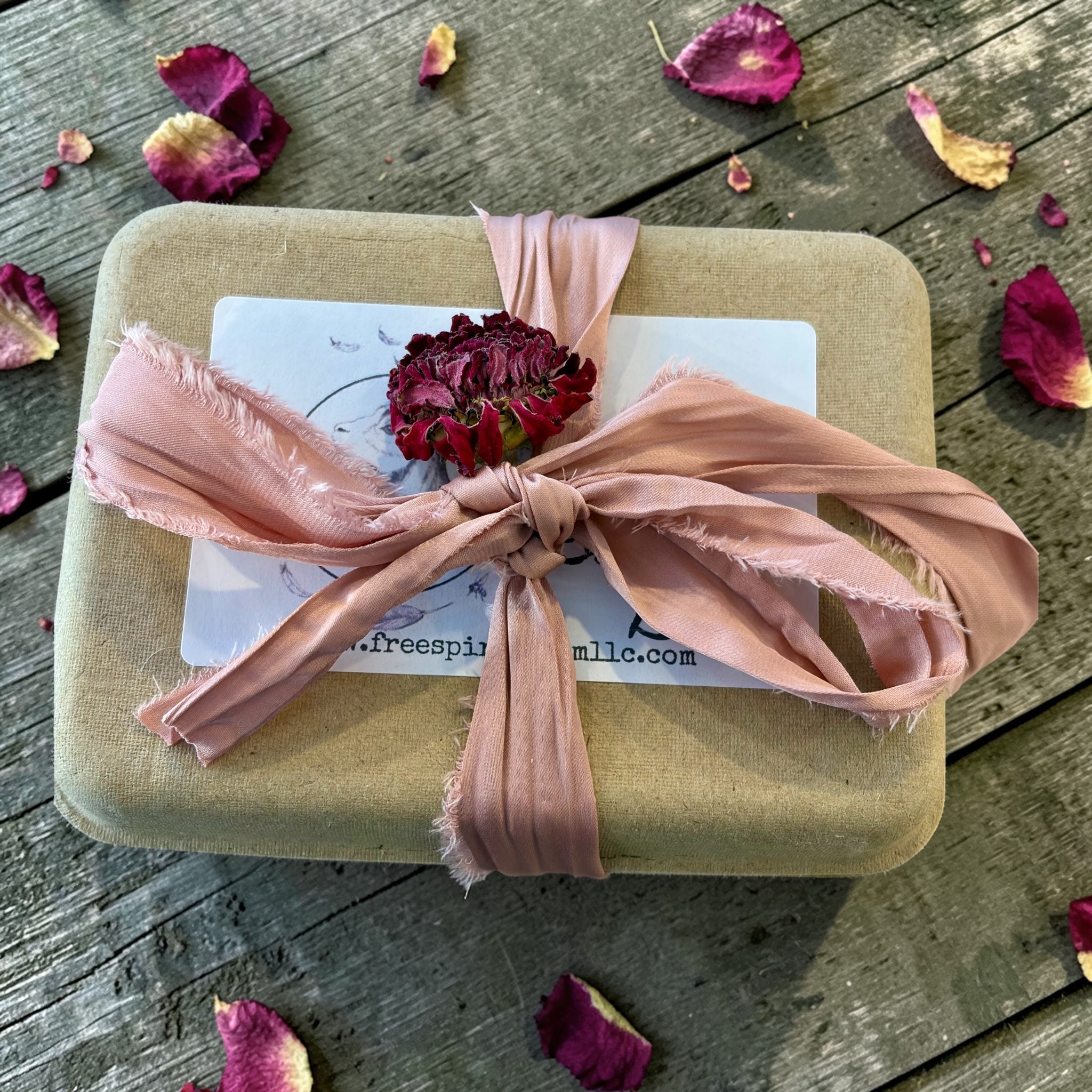 Gift box with pink ribbon and dried flowers on a wooden surface with petals scattered around