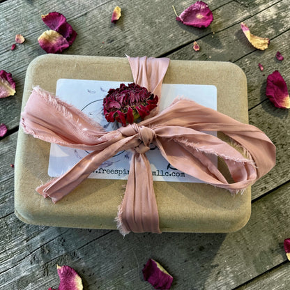 Gift box with pink ribbon and dried flowers on a wooden surface with petals scattered around