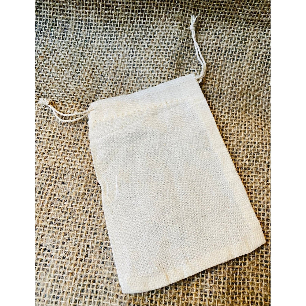A beige cotton muslin soap bag placed on a textured surface.