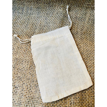 A beige cotton muslin soap bag placed on a textured surface.