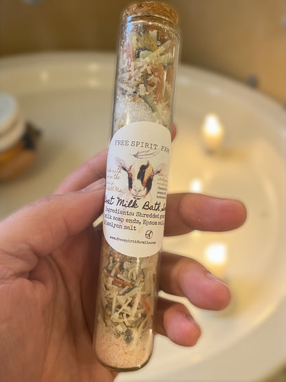 Hand holding a bottle of goat milk bath soak with a label, against a blurred bathroom background.