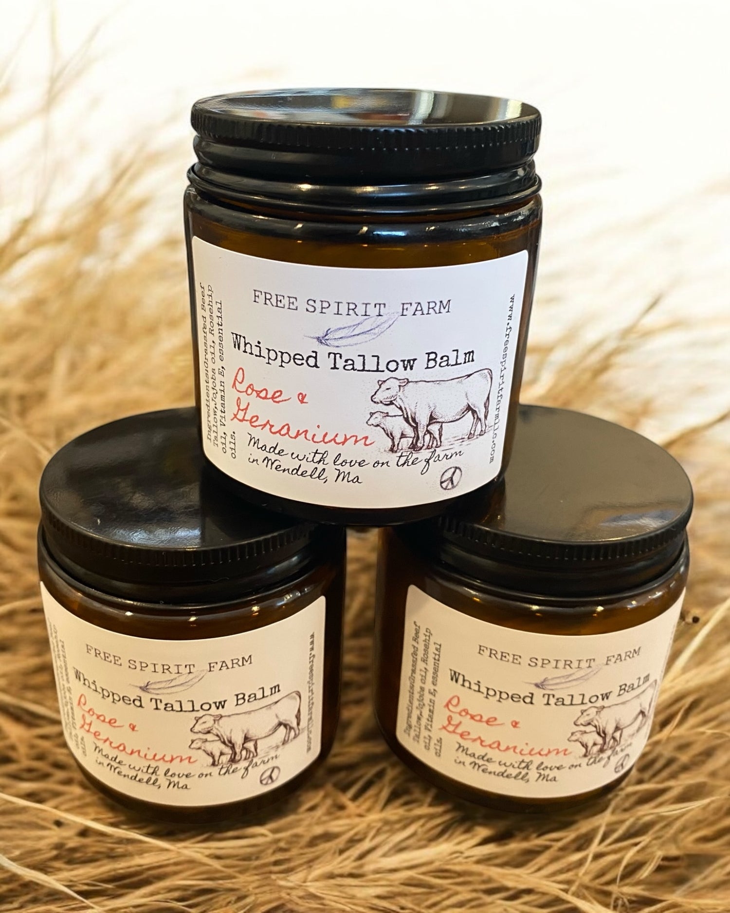 Three jars of Whipped Tallow Balm with labels indicating the product and scent, stacked on a straw-like surface.