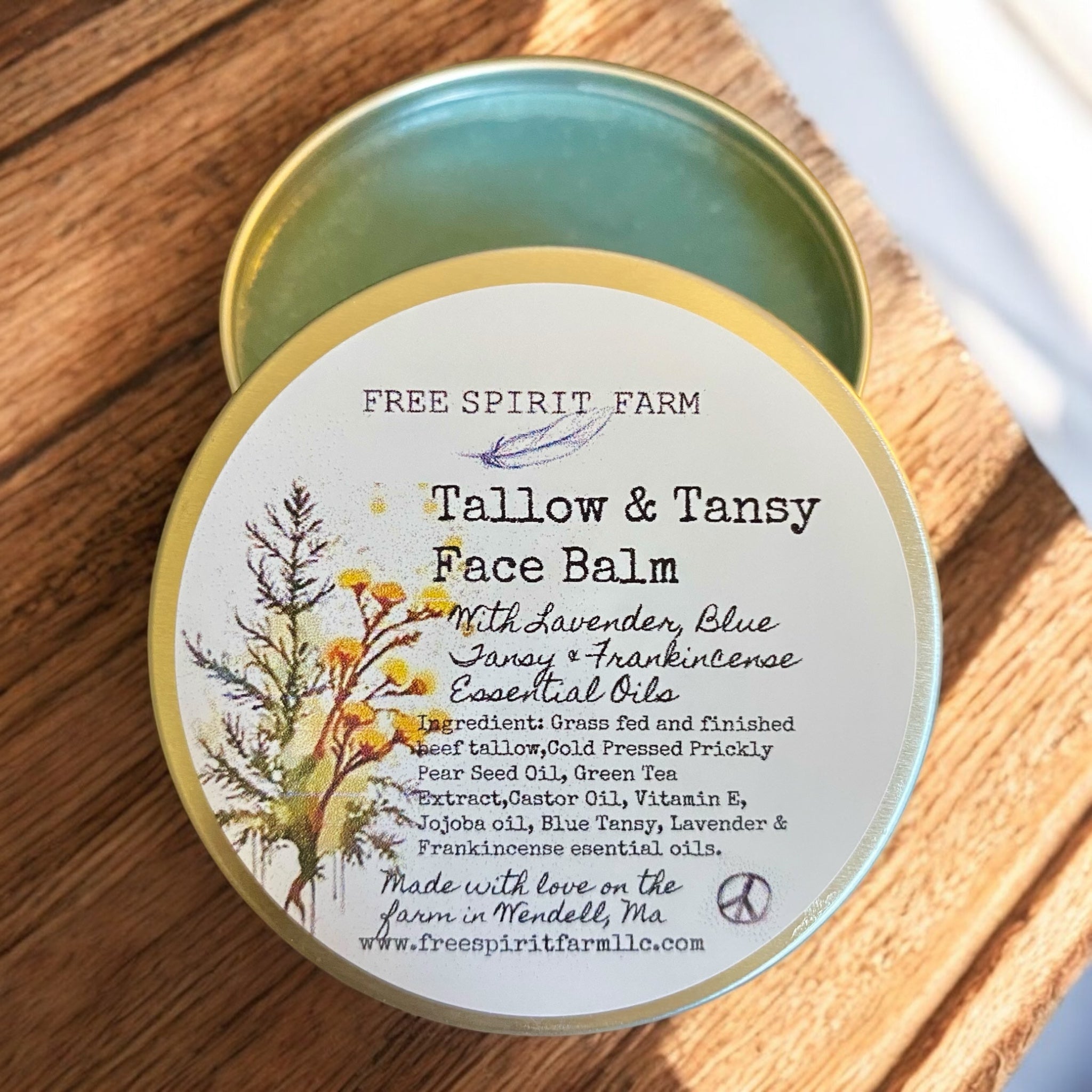 A tin container of Tallow &amp; Tansy Face Balm with a label featuring illustrations of plants and text detailing the product&