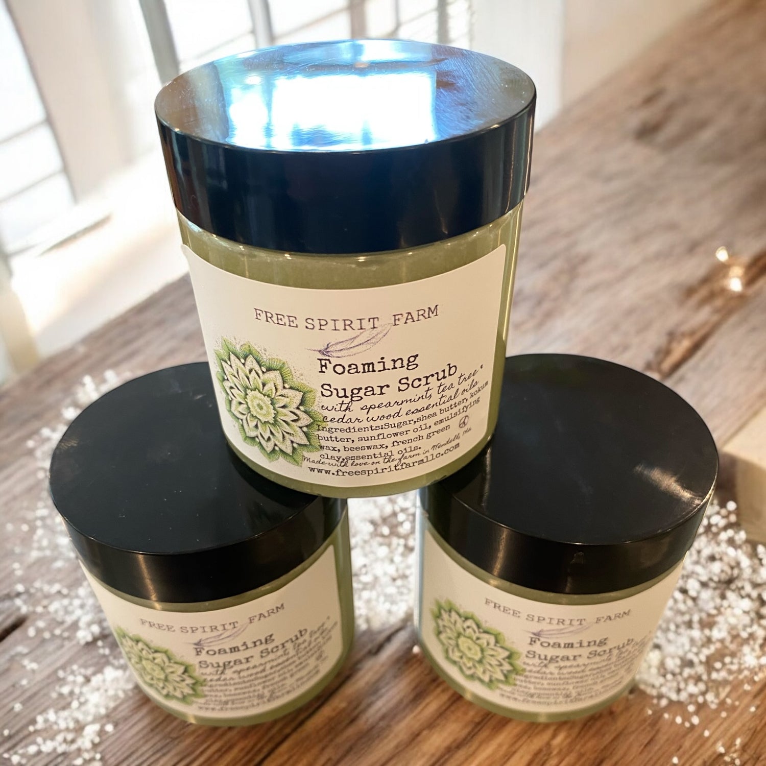 Three jars of Free Spirit Farm Foaming Sugar Scrub on a wooden surface.