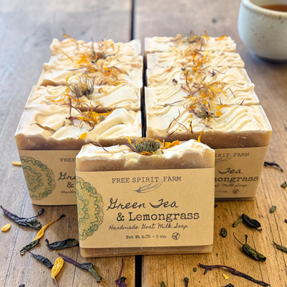 Three bars of Free Spirit Farm Green Tea &amp; Lemongrass soap on a wooden surface with tea leaves.