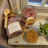 Two jars of bath salts with wooden spoons on a rustic surface, featuring Free Spirit Farm branding.