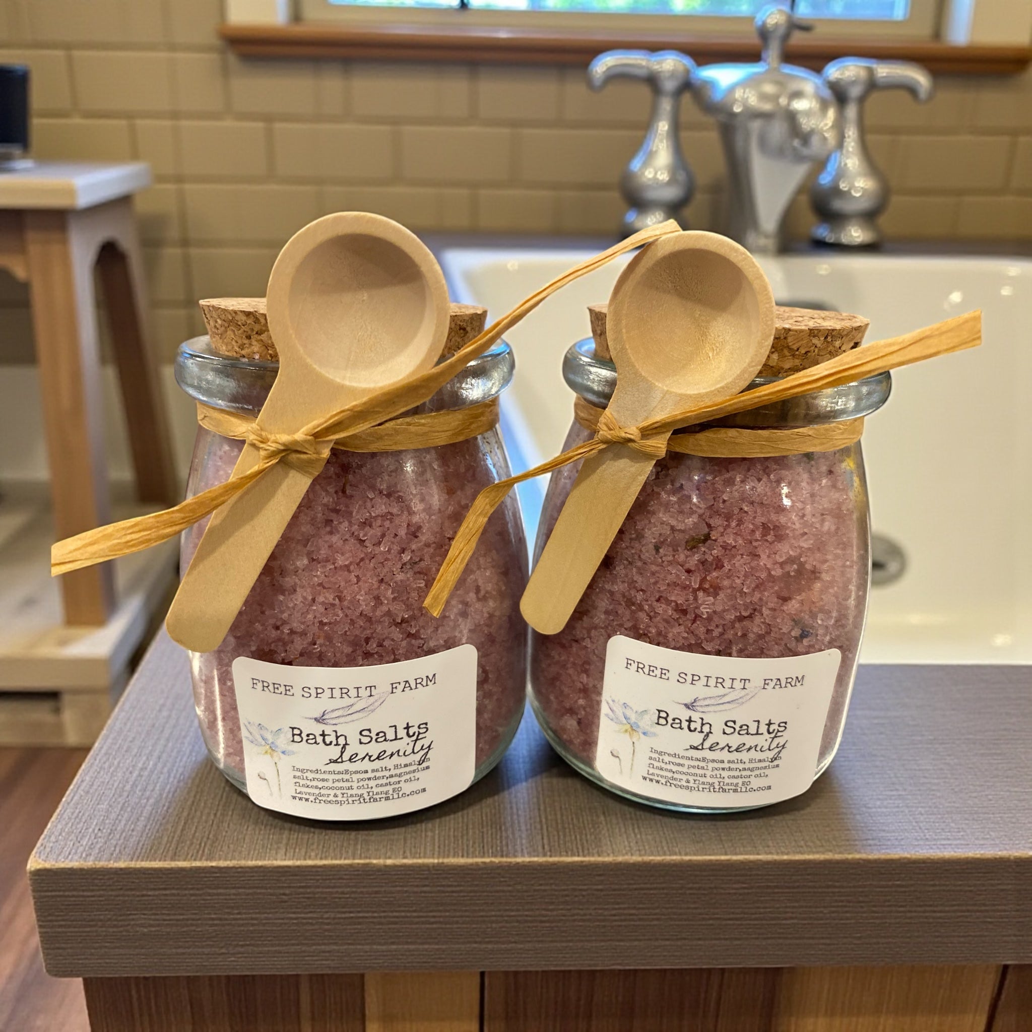 Two jars of bath salts with wooden spoons on a bathroom counter.