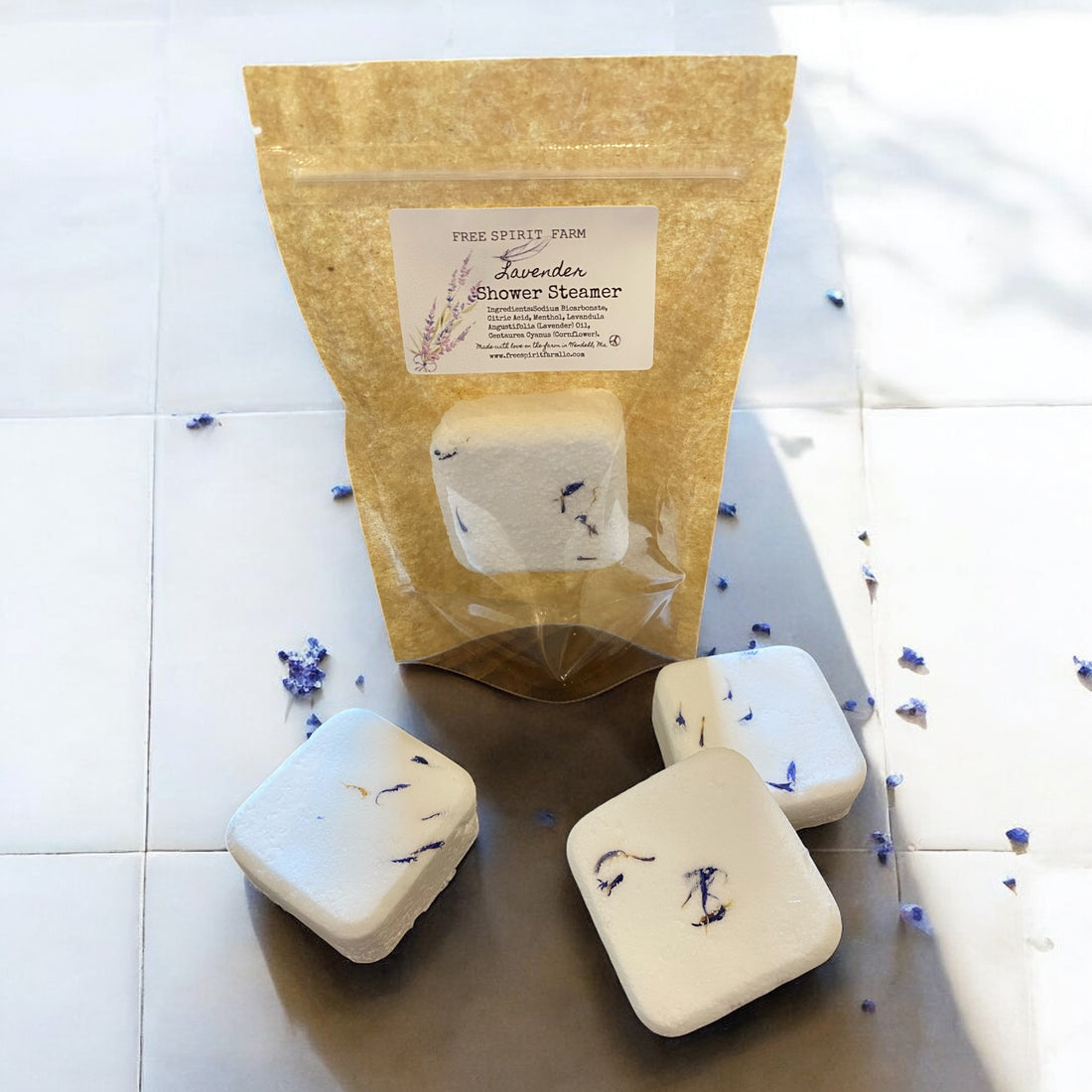 Four lavender shower steamers with a brown paper bag on a white tiled background