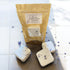 Four lavender shower steamers with a brown paper bag on a white tiled background
