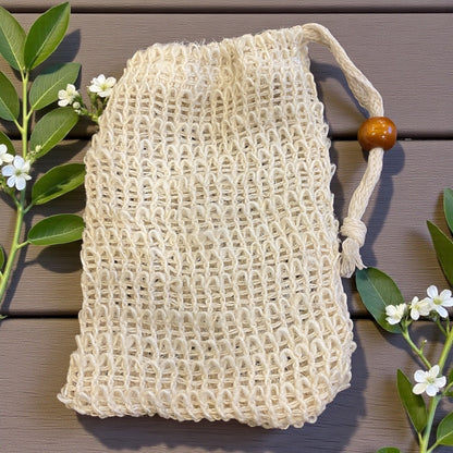 Beige mesh bag with a wooden handle on a wooden surface with green leaves and flowers.