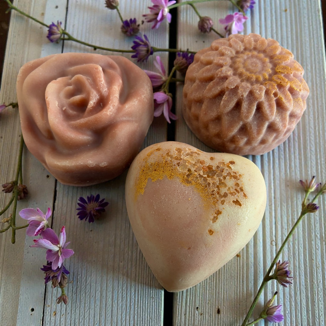 Three handmade soap bars with different shapes and designs on a wooden surface with flowers.