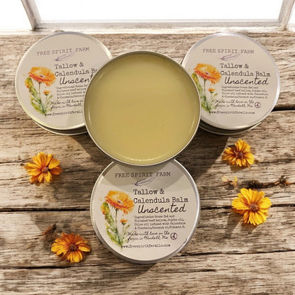 Three tallow and calendula balm containers on a wooden surface with flowers around.