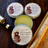 Three tins of Free Spirit Farm Tallow Beard & Hair Balm on a wooden surface with a map and bottle.
