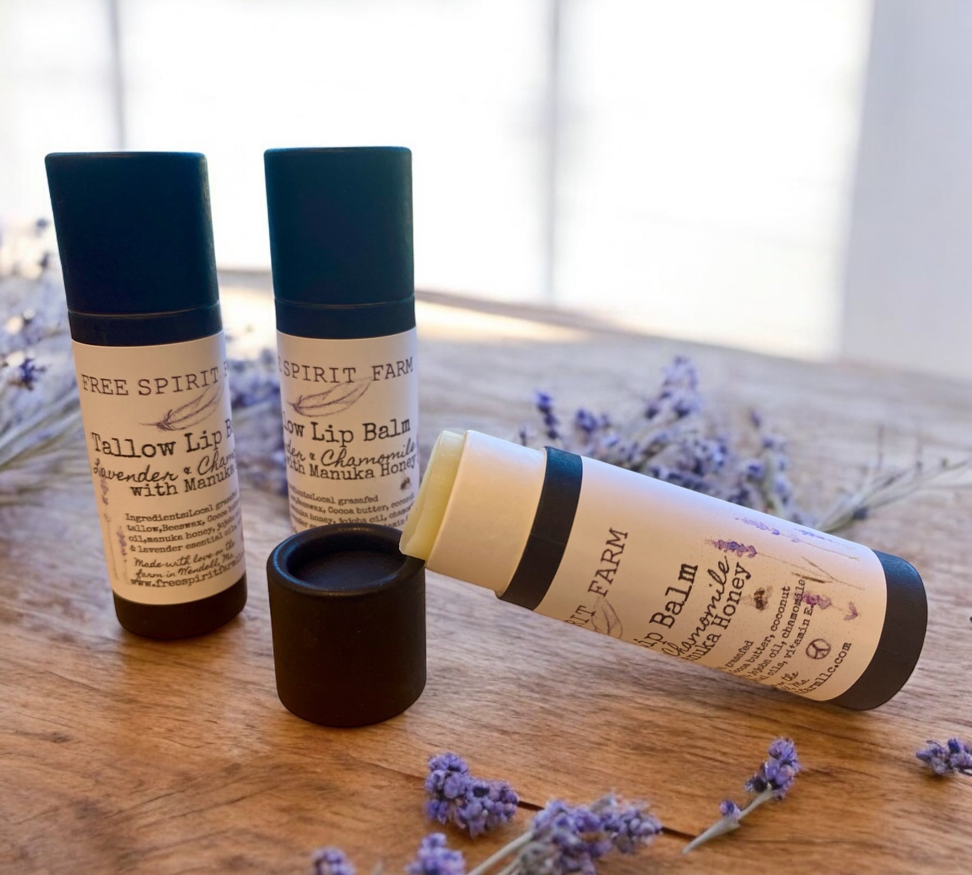 Three tubes of Tallow Lip Balm in a cardboard recyclable packaging, with lavender plants in the background.