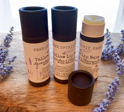 Three tubes of Tallow Lip Balm in a cardboard recyclable packaging, with lavender plants in the background.