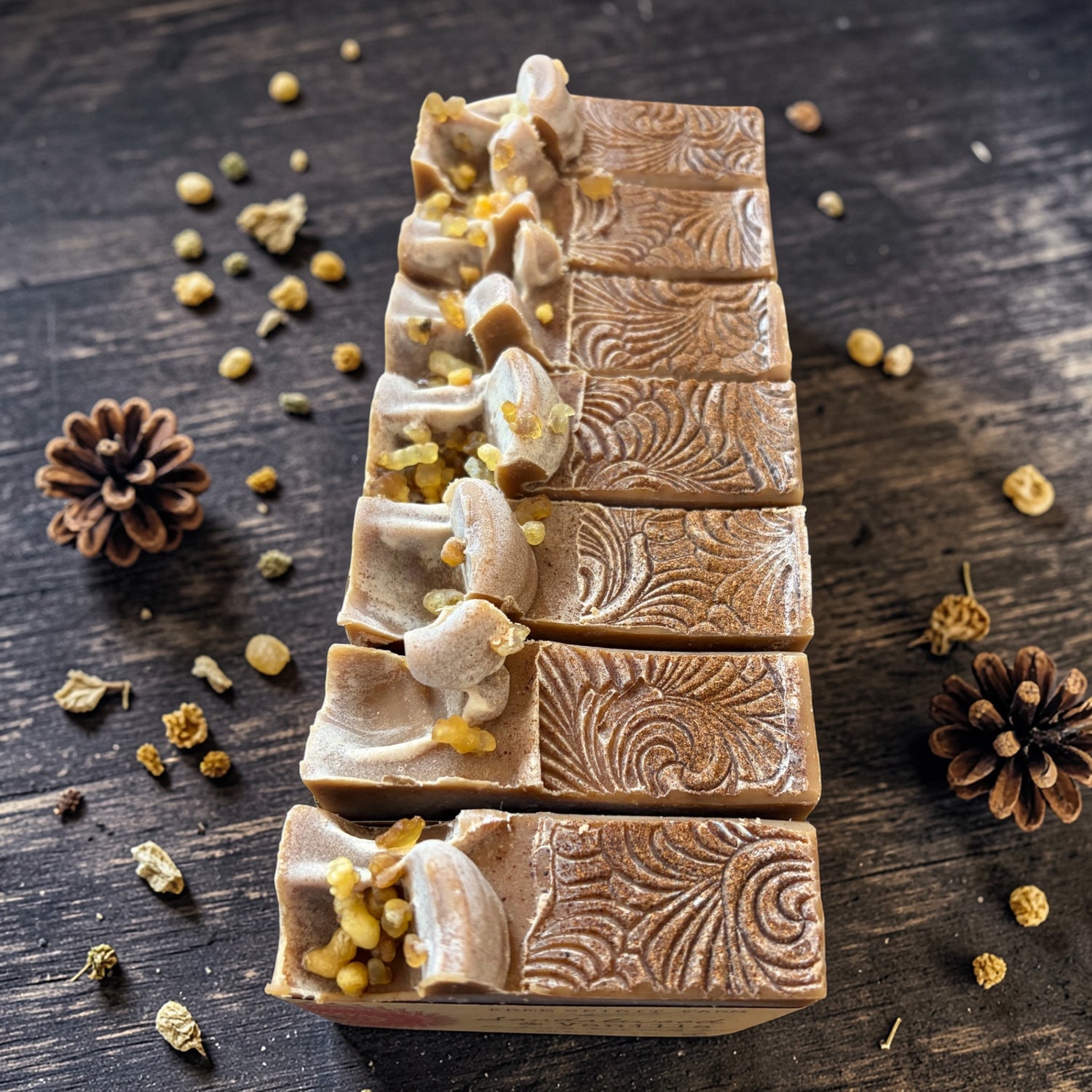 Decorative soap bars with intricate designs on a wooden surface with pine cones and herbs.
