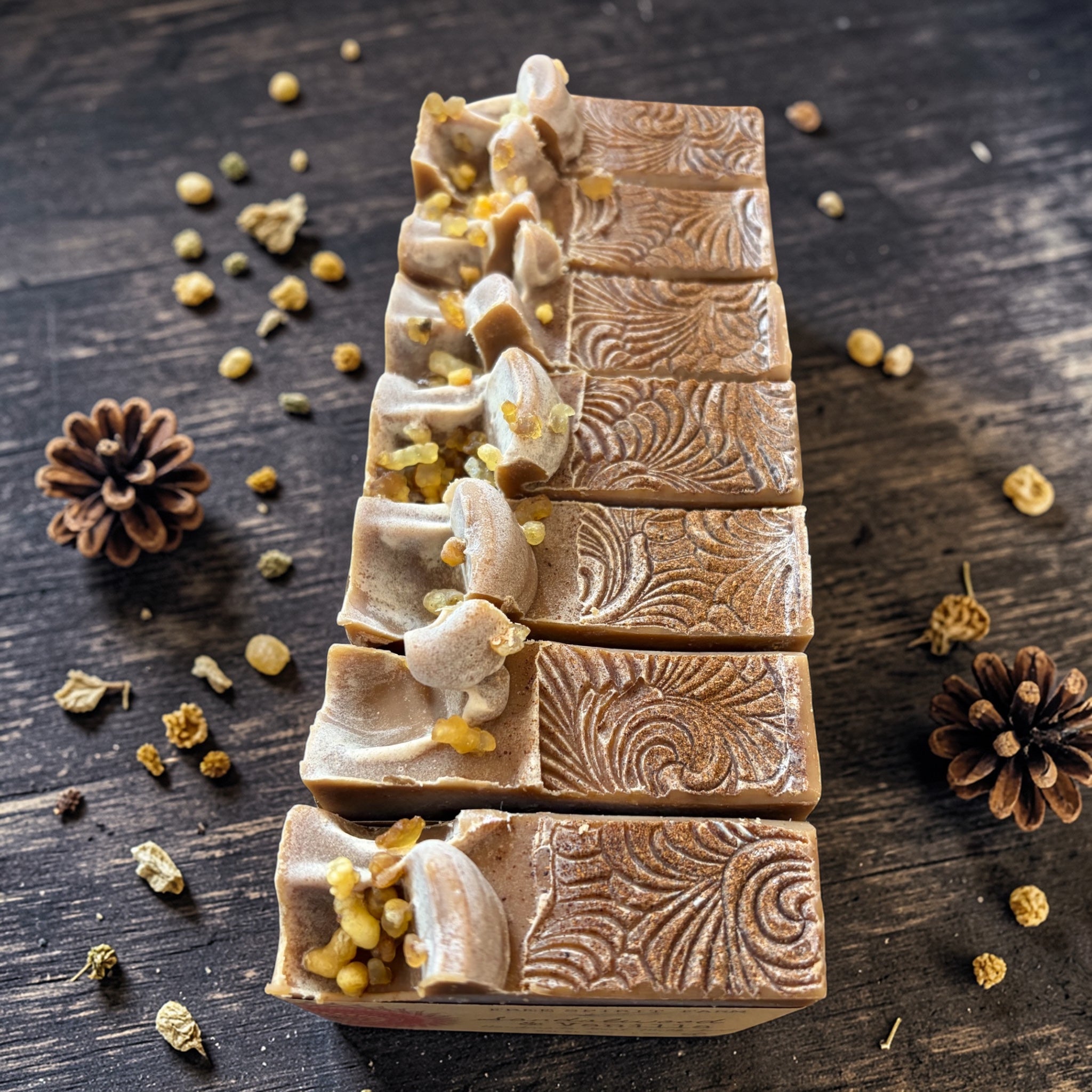 Decorative soap bars with intricate designs on a wooden surface with pine cones and herbs.