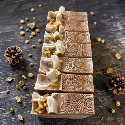 Decorative soap bars with intricate designs on a wooden surface with pine cones and herbs.