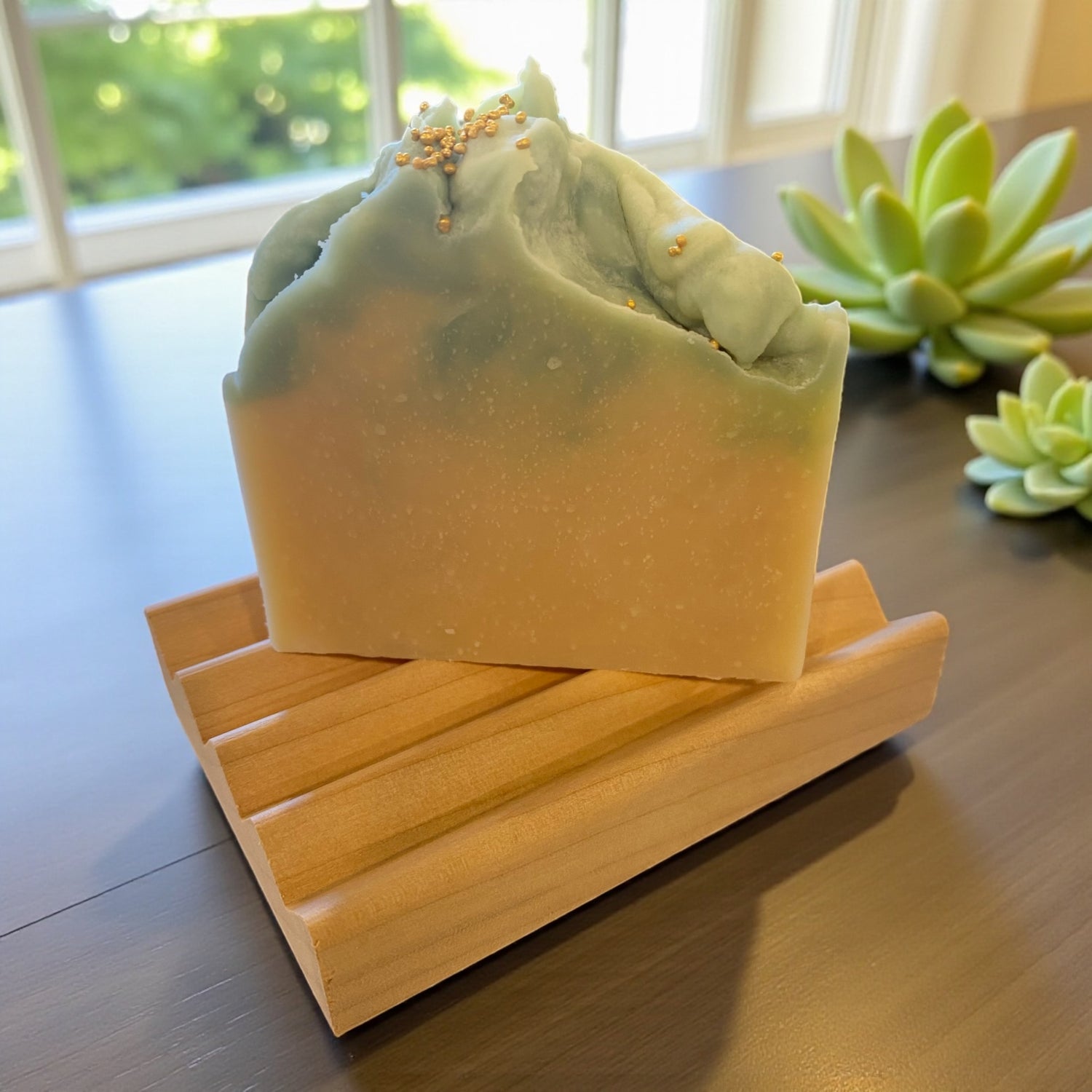 Green soap bar on a wooden soap dish with succulents in the background