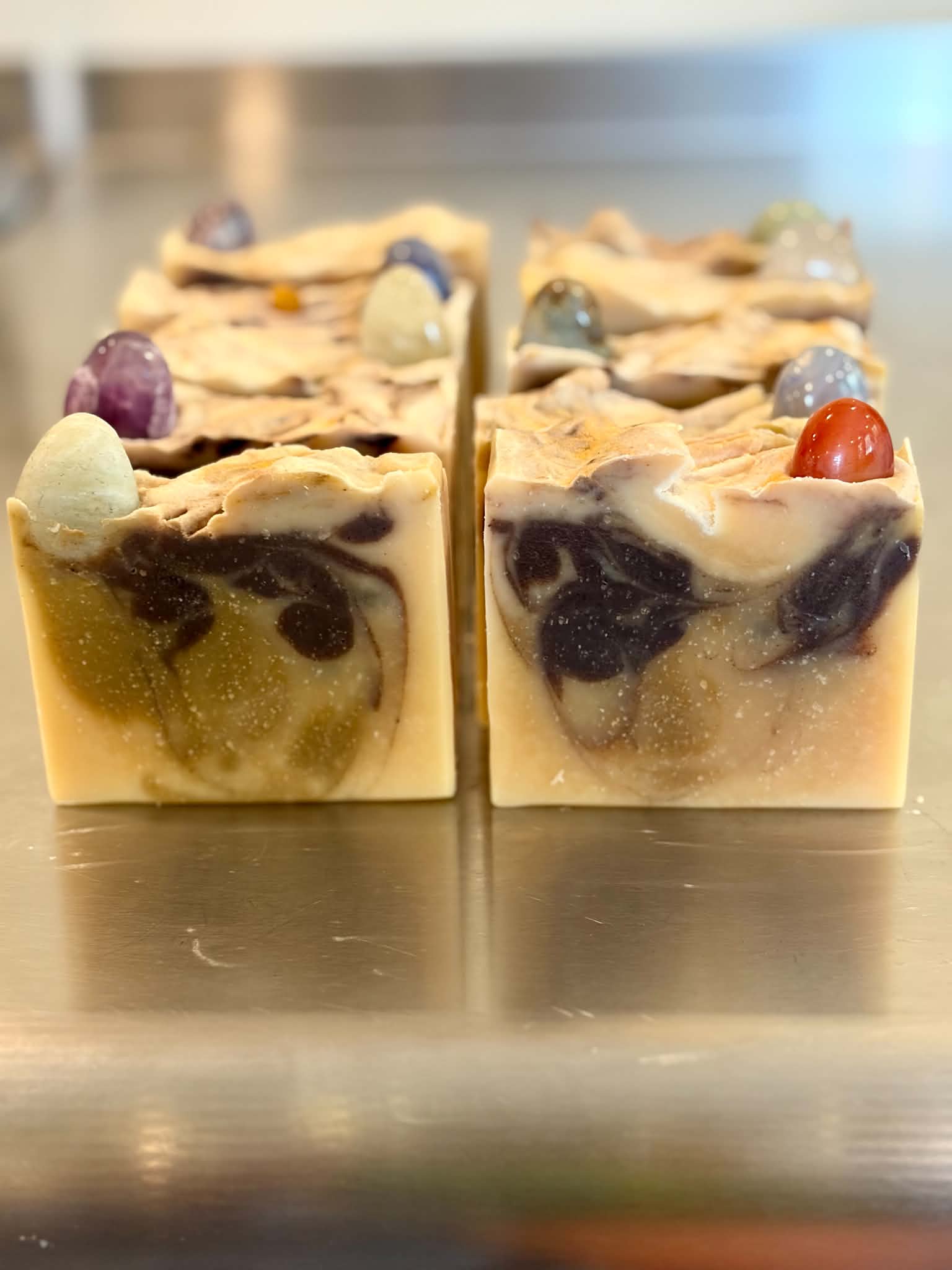 Free Spirit Farm bars of artisanal goat milk soap arranged on a reflective metallic surface. gem stone soap.